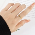 Minimalistischer Goldring mit grünem Zirkon am Zeigefinger vor einem Buchhintergrund - US 5 / Gold mit grünem Stein