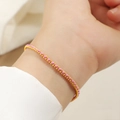 Detail eines filigranen geflochtenen roten Armbands mit polierten Gold-Titanstahlperlen - Gold Rosa Schnur