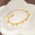 Detail of gold bean tassel bracelet with lobster clasp and adjustable chain on ceramic plate - Gold