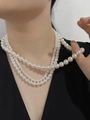Detalle de un collar de perlas de tres capas usado sobre un top negro con cuello en V - Collar de 10.0mm