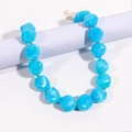 Dettaglio di perle blu marmorizzate su catena dorata esposte su un supporto cilindrico - Blu lago