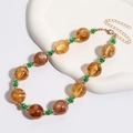 Macro-opname van vintage amberkleurige kralen met groene tussenringen en gouden sluiting - KC Goud / Amber