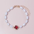 Elegant white rice pearl bracelet featuring a red clover charm and gold-tone lobster clasp - Red