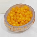 Close-up of translucent orange carnelian glass beads in a stone textured bowl - 4mm / Topaz Yellow