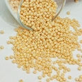 Macro-opname van crèmekleurige glazen kralen die uit een glas stromen voor DIY-sieraden - Beige