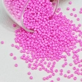 Macro-opname van roze glazen kralen die uit een pot worden gegoten voor DIY-sieraden - Lichtroze
