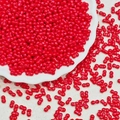 Macro detail of red twin-hole peanut glass beads for DIY jewelry in a white ceramic dish - Red