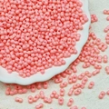 Macro detail of 3x6mm pastel pink glass seed beads in a white porcelain dish - Dusky Pink