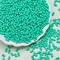 Macro detail of mint green peanut-shaped glass beads in a white decorative tray - Cyan Blue