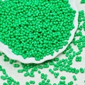 Macro shot of 3x6mm green peanut glass beads for jewelry making in white ceramic dish - Grass Green