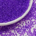 Macro view of translucent 3mm purple glass seed beads scattered near a white porcelain bowl - Dark Purple (3mm)