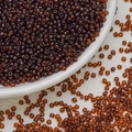 Detailed close-up of 3mm amber glass seed beads on a white ceramic plate for DIY jewelry - Dark Coffee
