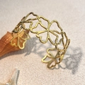 Goldenes Edelstahl-Manschettenarmband mit floralem Ausschnitt auf Strandhintergrund - Gold