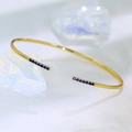 Minimalistischer vergoldeter Armreif mit dunkelblauen Zirkonia-Steinen auf weißem Grund - Gold Blauer Zirkon