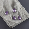 Macro shot of purple pear-shaped zircon charms with silver settings on a grey stone - Dark Purple Style (M110606)