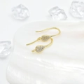 Elegante gouden druppeloorbellen met zirkonia op een witte schelp en kristallen achtergrond - Goud