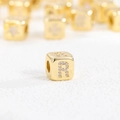 Makro-Detail von vergoldetem Würfel-Charm mit Zirkonia und graviertem Buchstaben R - Buchstabe R