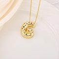Gros plan du pendentif lettre G dorée avec zircons colorés sur un fond en soie - Lettre G