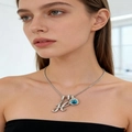 Macro detail of silver necklace featuring rhinestone letter K and blue square gemstone - Silver H