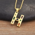 Primer plano del colgante letra H dorado con piedras de circonia de colores y fondo natural - Letra H