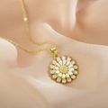 Macro view of white enamel sunflower pendant with gold petals on soft fabric - White
