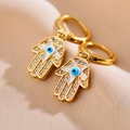 Macro-opname van gouden Hamsa-hand oorbellen met Evil Eye en kristallen op beige stof - Gepaveerde Hand van Fatima Stijl