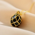 Macro detail of egg-shaped black enamel pendant with golden grid on silk background - Black