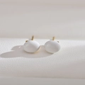 Macro shot of minimalist white oval pearl studs with golden posts on leather texture - White