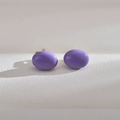 Macro view of purple oval stud earrings with a glossy finish and golden metal pins - Purple