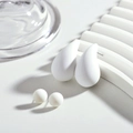 Vue macro de boucles d'oreilles goutte blanches mates et de puces sur décor épuré - Blanc