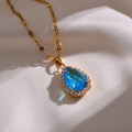 Elegante gouden ketting met peervormige blauwe kristallen hanger en diamanten halo - Blauw