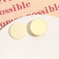 Macro shot of 26mm matte cream yellow resin round stud earrings on a textured plate - Off White