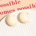Detail von halbmondförmigen Harzohrringen mit cremiger Marmorierung auf weißem Tablett - Beige