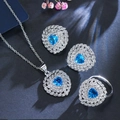 Elegante sieradenset met blauwe hartkristallen en micro-pave veren op blauwe achtergrond - Aquamarijn