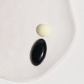 Close-up of cream round and black oval resin beads on a minimalist white ceramic tray - White Half Ball + Black Oval