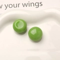 Macro shot of two glossy bright green resin cabochons on a white textured ceramic plate - Green