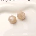 Macro shot of 16mm beige starfield resin beads with cat-eye luster on a white tray - Off-white