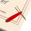 Macro view of transparent red jelly teardrop pendant with gold needle on a book - Large / Red