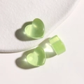 Macro shot of three translucent green resin heart charms on a white ceramic plate - Green