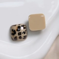 Detail van vierkante luipaard- en beige harsbedeltjes op een wit keramisch bordje - Vierkant / Wit Koffie