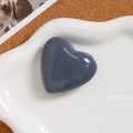 Close-up of a glossy dark grey heart pendant on a white tray with a cork background - Gray