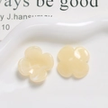 Macro detail of creamy yellow resin clover flower charms on a wavy ceramic tray - Off White