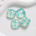 Close-up of four square resin patches with blue and white checkered patterns in a white tray - Blue