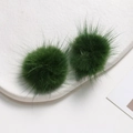 Close-up of fluffy dark green mink fur pompom balls on a minimalist white ceramic tray - Green