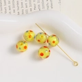 Macro detail of 10mm yellow glass beads with colorful dots and gold jewelry pins - Yellow