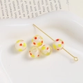 Detail shot of five 10mm dotted glass beads and a gold pin in a white heart dish - White