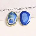Makro-Detail asymmetrischer Harzohrringe mit blauen Blumen, Perlen und goldenem Metallrand - Dunkelblau Trockenblume