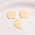 Macro detail of three glossy cream square resin charms on a white ceramic display tray - Pure White