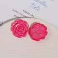 Makroansicht von zwei magentafarbenen Harzrosenanhängern für DIY-Schmuck auf weißer Keramik - Fuchsia