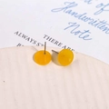 Detailed close-up of yellow acrylic round stud earrings on a textured ceramic plate - Yellow